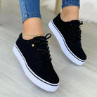 Women's black casual sneakers with white soles, lace-up design, worn with blue jeans. Stylish, versatile footwear for spring fashion 2023.