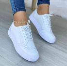 White lace-up women's sneakers with brogue detailing, worn with blue jeans. Stylish, versatile casual footwear for spring 2023 fashion trends.