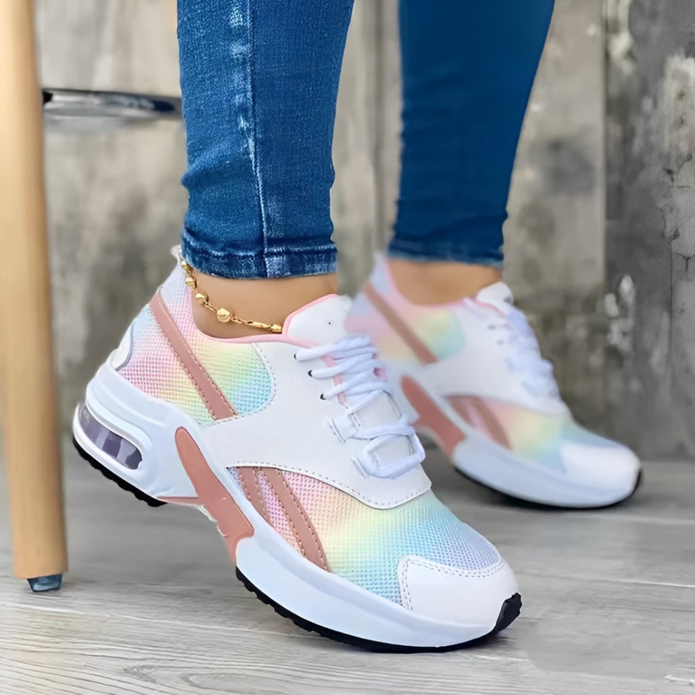 Colorful women's sneakers with rainbow gradient design, white laces, and pink accents, worn with blue jeans. Fashionable casual footwear.