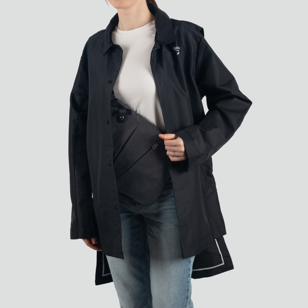 Person wearing a black raincoat over a white shirt and blue jeans, holding a black crossbody bag. Fashionable outerwear and accessories.