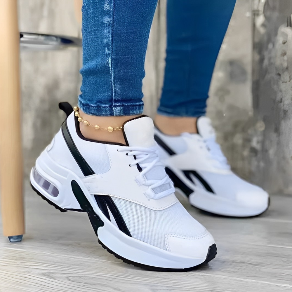 White athletic sneakers with black accents on a wooden floor, worn with blue jeans. Stylish, comfortable footwear for casual and sports activities.