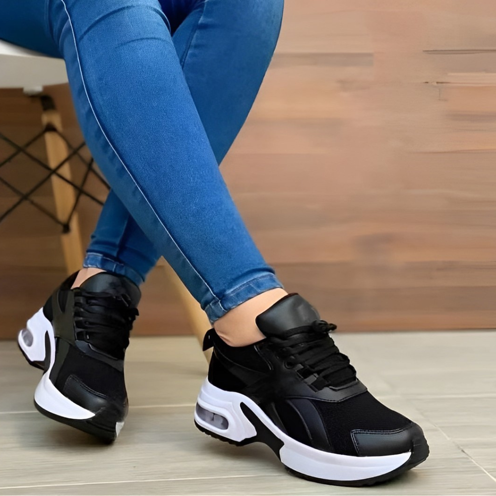 Black and white athletic sneakers on person wearing blue jeans, sitting on a chair. Stylish casual footwear, modern design, comfortable fit.