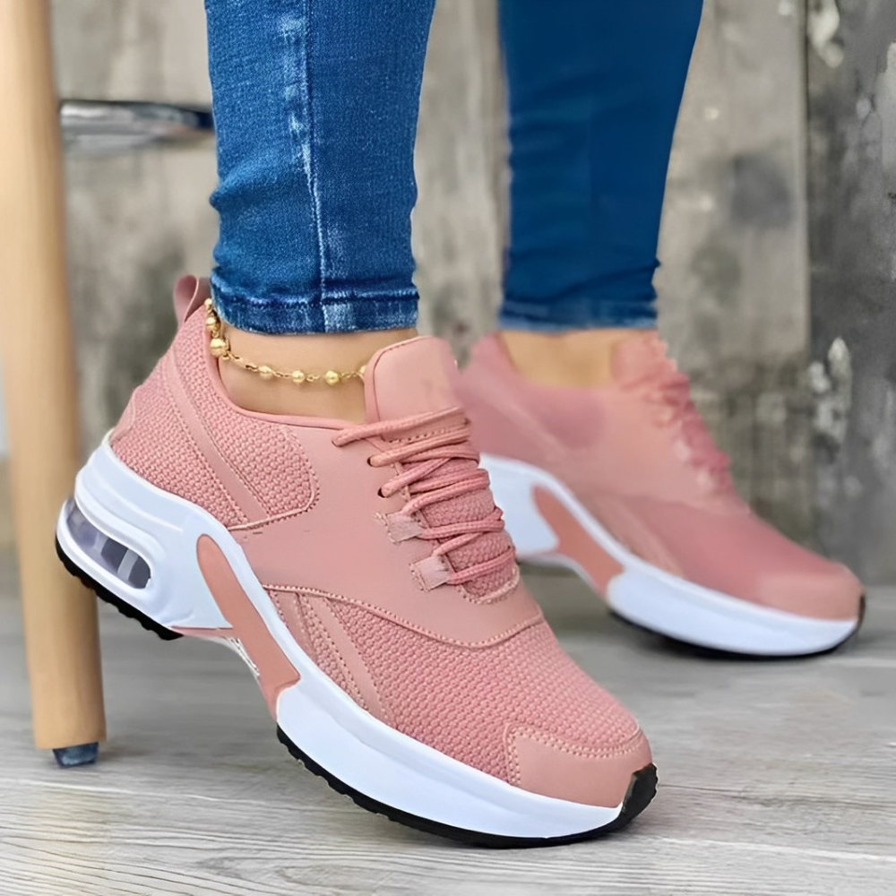 Pink women's athletic sneakers with white soles, worn with blue jeans. Stylish, comfortable footwear for casual wear or running. Fashionable sports shoes.