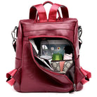 Red leather backpack with multiple compartments, showcasing organized storage for essentials like a water bottle, phone, and wallet. Stylish and functional design.