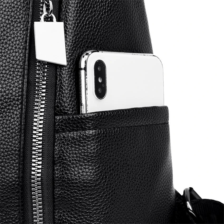 Black leather backpack with silver zipper and front pocket holding a smartphone. Stylish, durable, and functional accessory for travel or daily use.