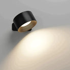 Modern black wall sconce with circular design, casting warm light on a gray wall. Ideal for contemporary home lighting and interior decor.