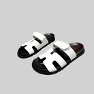 White leather sandals with black soles, featuring a double strap design and open toe, perfect for casual summer wear. Stylish and comfortable footwear.