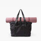 Black tote bag with pink yoga mat, featuring durable handles and spacious design. Ideal for gym, travel, or daily use. Stylish and functional accessory.