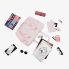 Pink tote bag with accessories including a smartphone, sunglasses, headphones, magazines, and makeup items on a white background. Fashion essentials display.