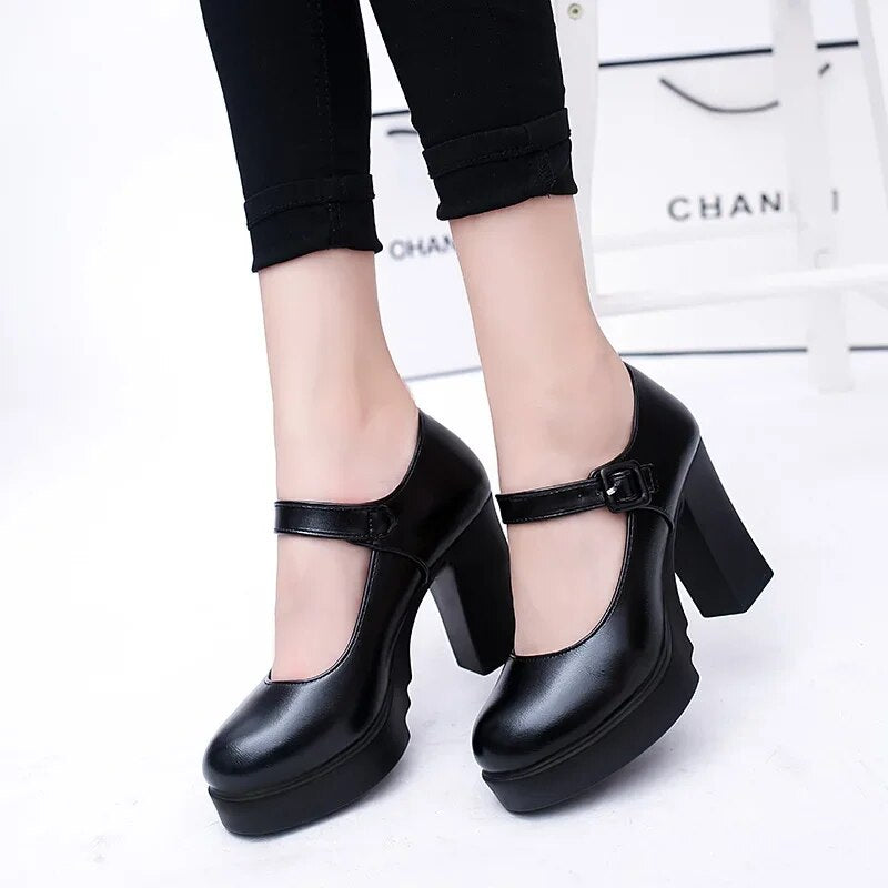 Black Mary Jane platform heels with ankle strap, worn with black pants. Stylish women's footwear, perfect for fashion-forward outfits and casual wear.