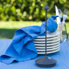 Modern black fly repellent fan on outdoor dining table with stacked white plates, blue napkin, and cutlery. Ideal for pest-free alfresco dining.