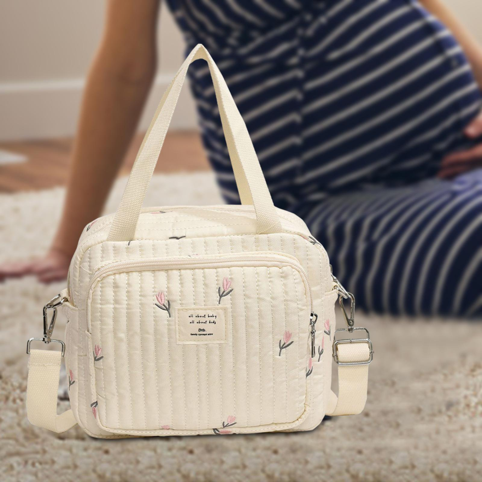 Quilted floral diaper bag with adjustable strap on a soft carpet, ideal for moms. Perfect for baby essentials, stylish and functional design.