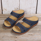 Women's navy blue wedge sandals with cutout design, double straps, and cushioned sole on rustic wooden background. Comfortable summer footwear.