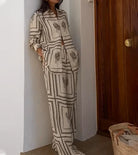 Woman wearing a stylish beige cactus print loungewear set, standing by a wooden door, with a woven basket bag on the floor. Fashionable home attire.