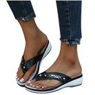 Women's black wedge flip-flops with white soles, featuring metallic accents, worn with frayed hem jeans. Stylish summer footwear for casual outings.