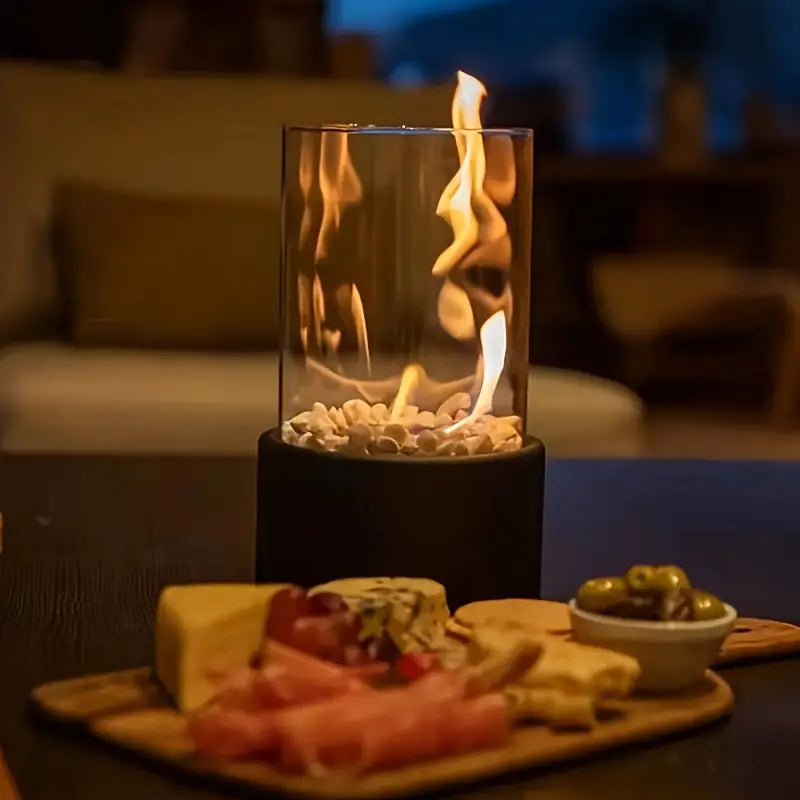 Tabletop fire pit with glass enclosure, surrounded by a cozy indoor setting. Features a charcuterie board with cheese, meats, and olives in the foreground.