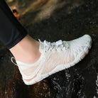 White minimalist water shoes with breathable mesh design, worn outdoors on wet rocks. Lightweight, quick-dry footwear ideal for hiking and aquatic activities.