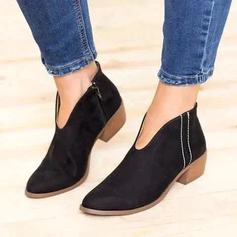 Black V-cut ankle boots with wooden block heels, worn with blue jeans. Stylish women's footwear, perfect for casual and trendy outfits.