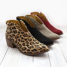 Four stylish ankle boots with block heels in leopard print, black, gray, and red, displayed on a white wooden floor. Fashionable women's footwear.