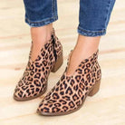 Leopard print V-cut ankle boots with block heels, worn with blue jeans on a wooden floor. Fashionable women's footwear, trendy style.