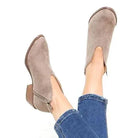 Women's taupe suede V-cut ankle boots with block heels, paired with blue jeans. Stylish fall footwear, perfect for casual outfits.