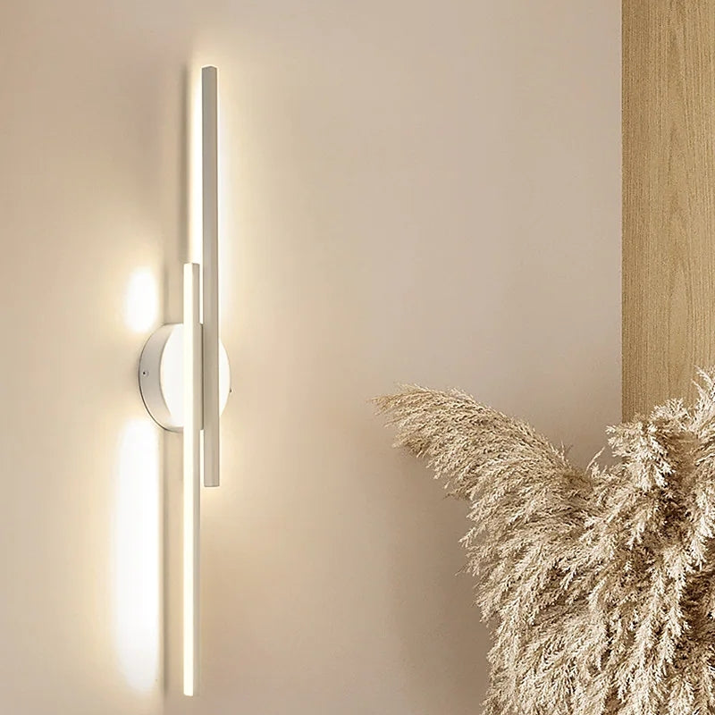 Modern LED wall sconce with sleek vertical design, emitting warm light on beige wall, complemented by decorative pampas grass. Ideal for contemporary interiors.