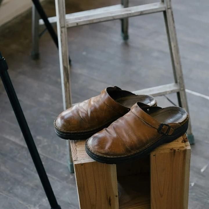 Brown leather clogs on wooden block, rustic footwear, vintage style shoes, casual slip-ons, wooden floor, metal ladder background.