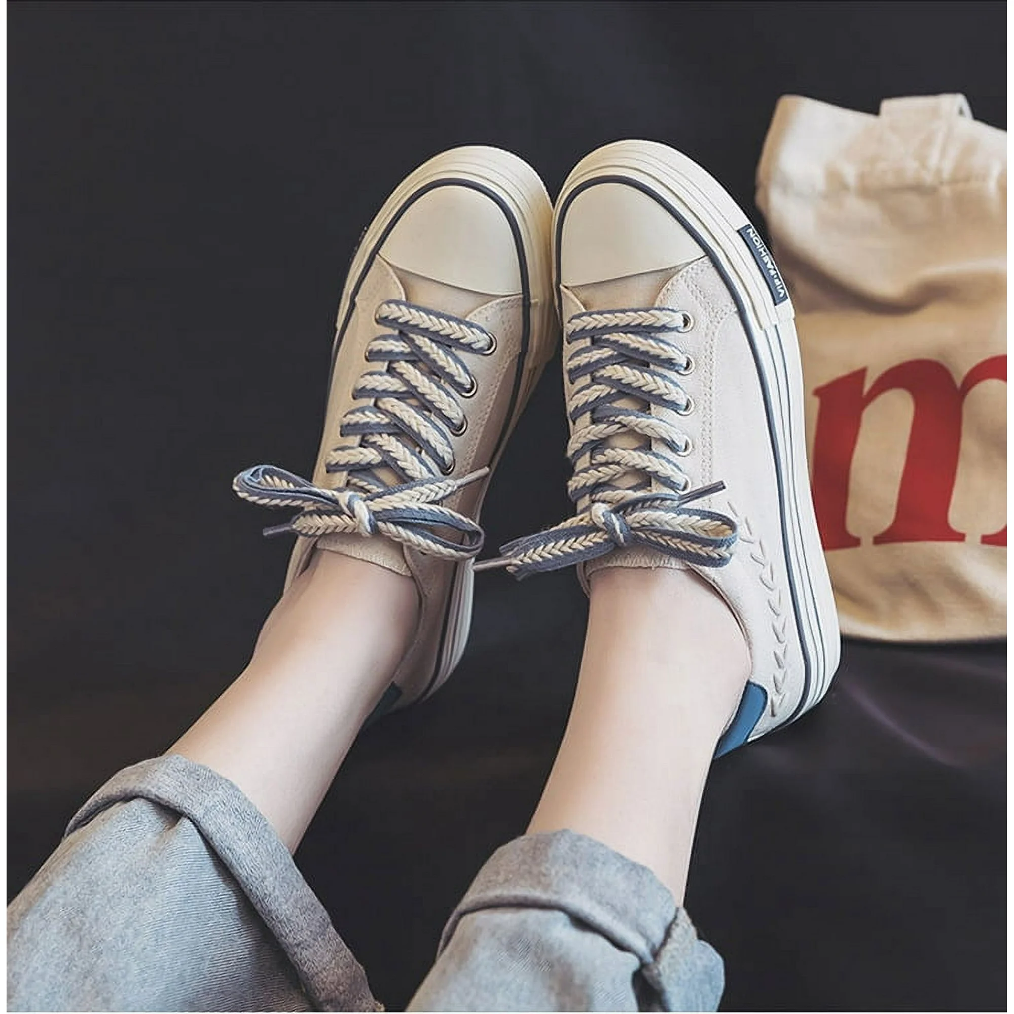 Casual beige canvas sneakers with blue accents and white rubber soles, featuring striped laces, worn with rolled-up jeans. Fashionable footwear.