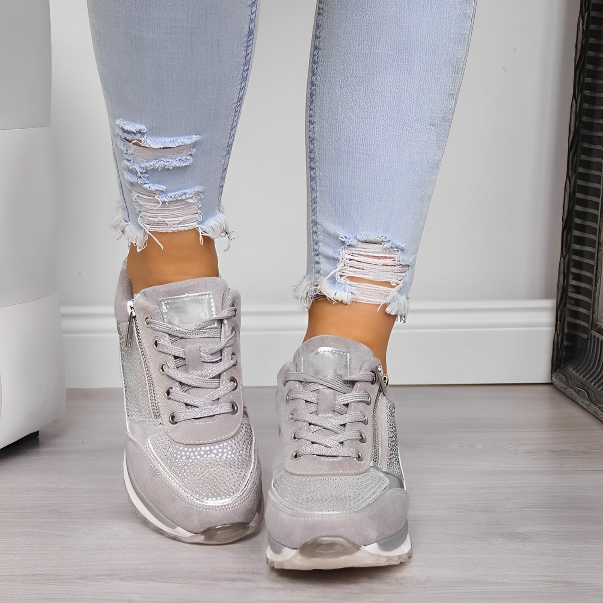 Stylish silver sneakers with rhinestone details paired with ripped light blue jeans on a wooden floor. Fashionable women's footwear and denim outfit.