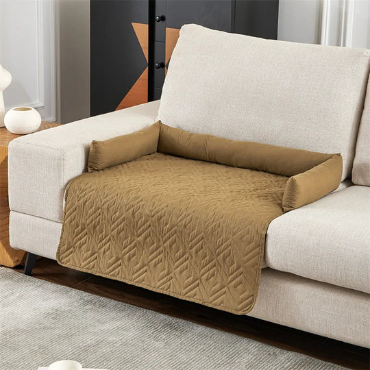 Beige quilted sofa protector on a light gray couch, featuring armrest covers and a textured pattern. Ideal for pet protection and furniture preservation.