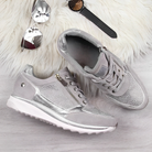 Stylish silver women's sneakers with metallic accents, side zipper, and textured sole on a wooden floor, accompanied by sunglasses and a watch.