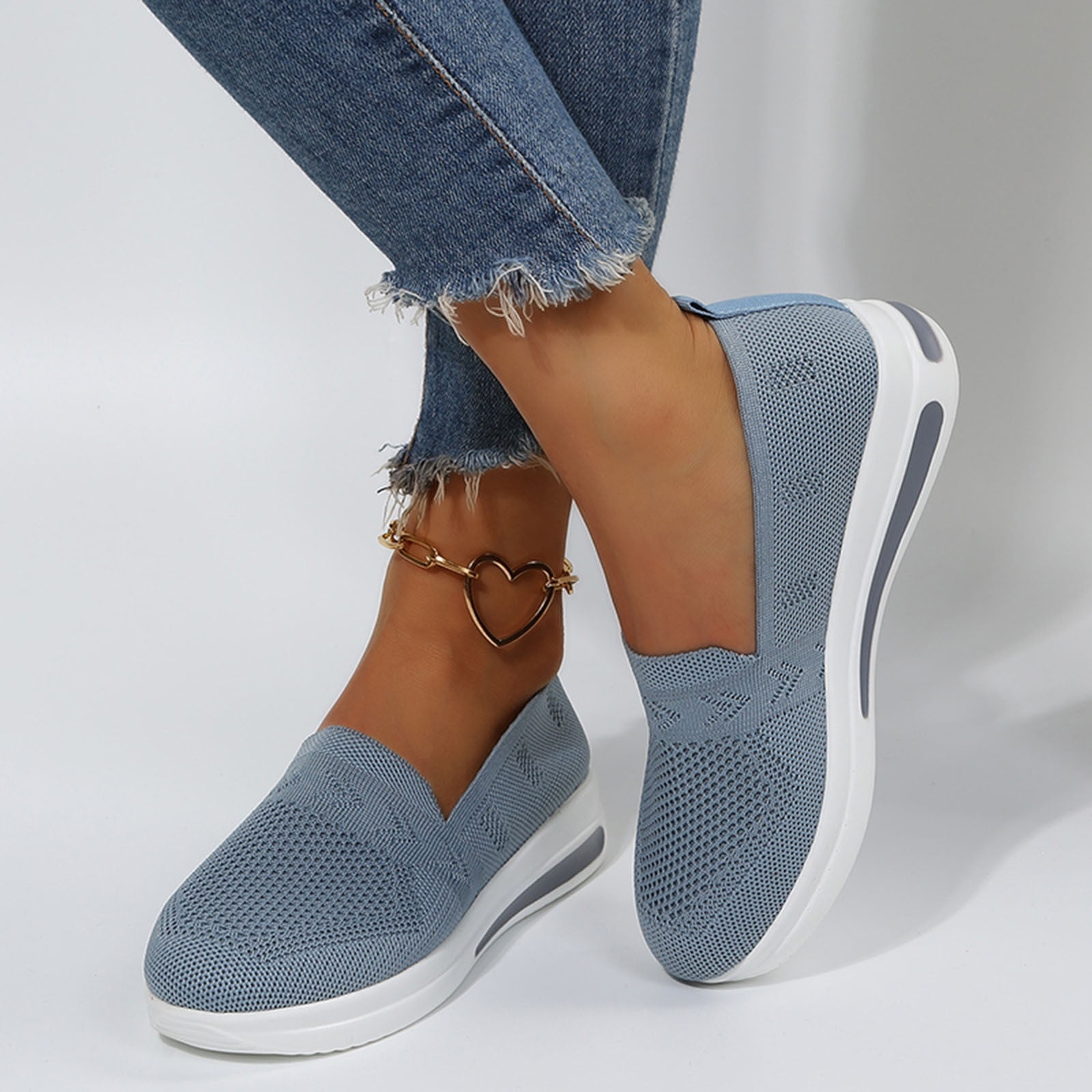 Blue slip-on sneakers with white soles, worn with frayed hem jeans and a heart-shaped anklet. Stylish women's casual footwear.