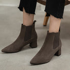 Women's brown suede ankle boots with block heels and elastic side panels, paired with black frayed hem jeans, on a neutral background.