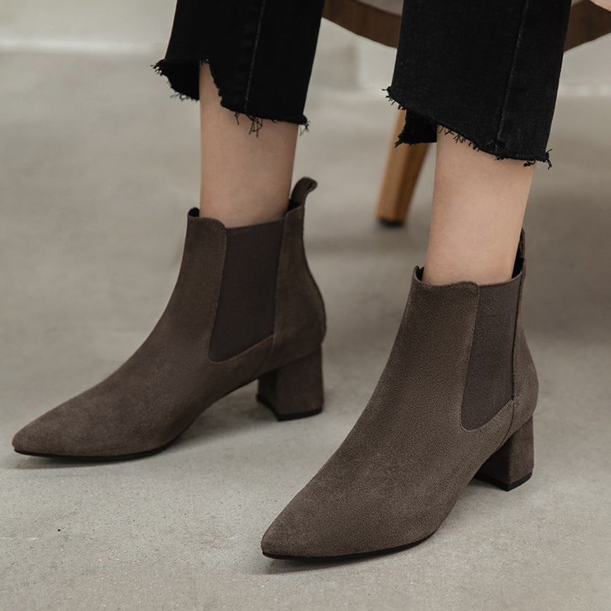 Women's brown suede ankle boots with block heels and elastic side panels, paired with black frayed hem jeans, on a light gray floor.