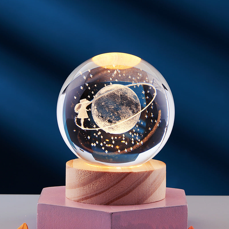 Crystal ball with 3D engraved planet and stars, illuminated on a wooden base. Perfect for home decor, gifts, and astronomy enthusiasts.