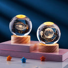 Glass galaxy crystal balls with LED lights on wooden bases, featuring cosmic designs and an astronaut, perfect for home decor or gifts.