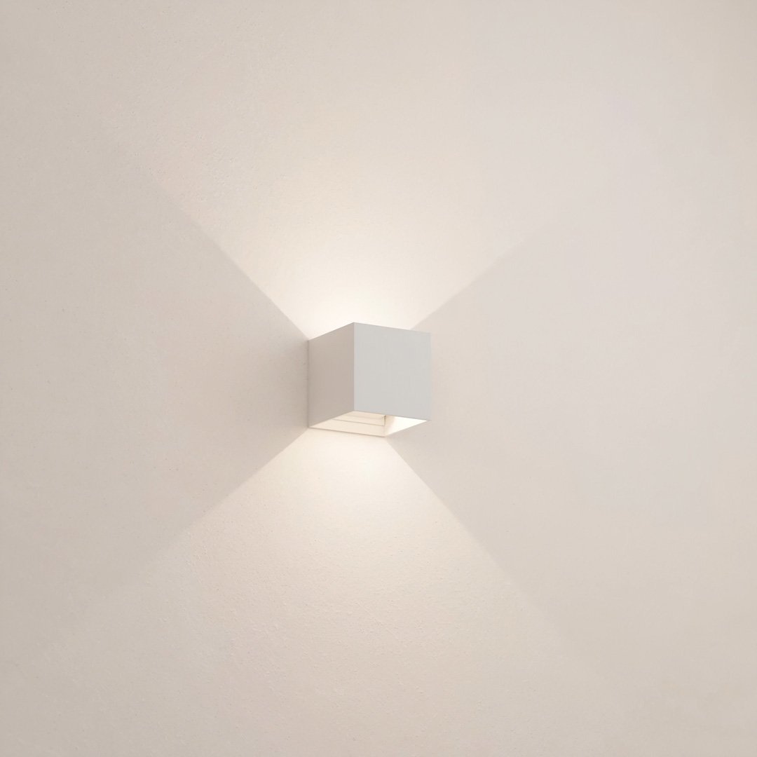 Minimalist white wall sconce emitting soft ambient light, modern cube design, interior lighting fixture, home decor, contemporary wall lamp.