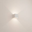 Minimalist white wall sconce emitting soft ambient light, modern cube design, interior lighting fixture, home decor, contemporary wall lamp.