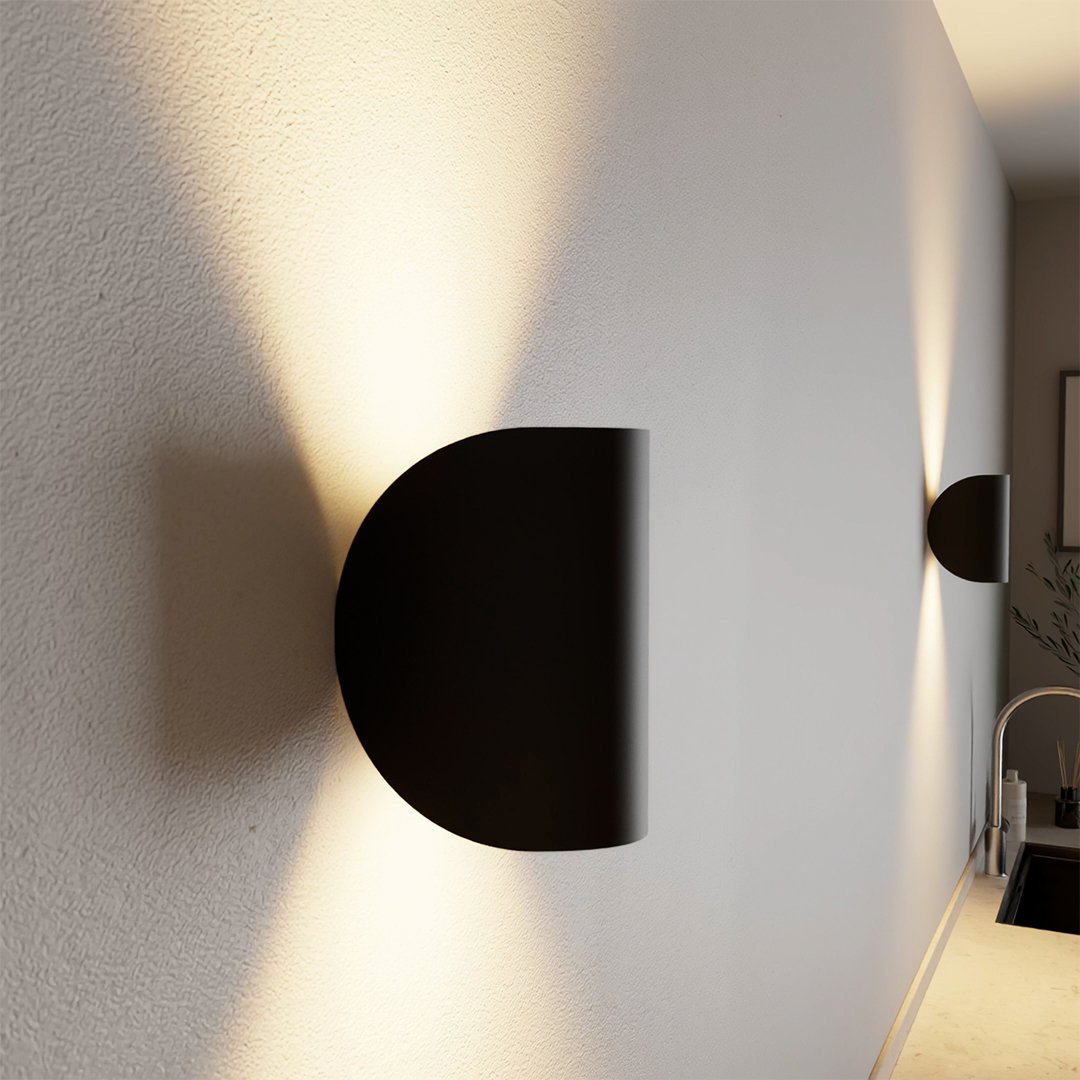 Modern black wall sconce with minimalist design, casting ambient light on a textured white wall. Ideal for contemporary home lighting decor.