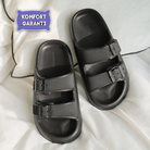 Black ergonomic sandals with adjustable straps on a white background, featuring a "Komfort Garanti" label. Comfortable footwear for everyday use.