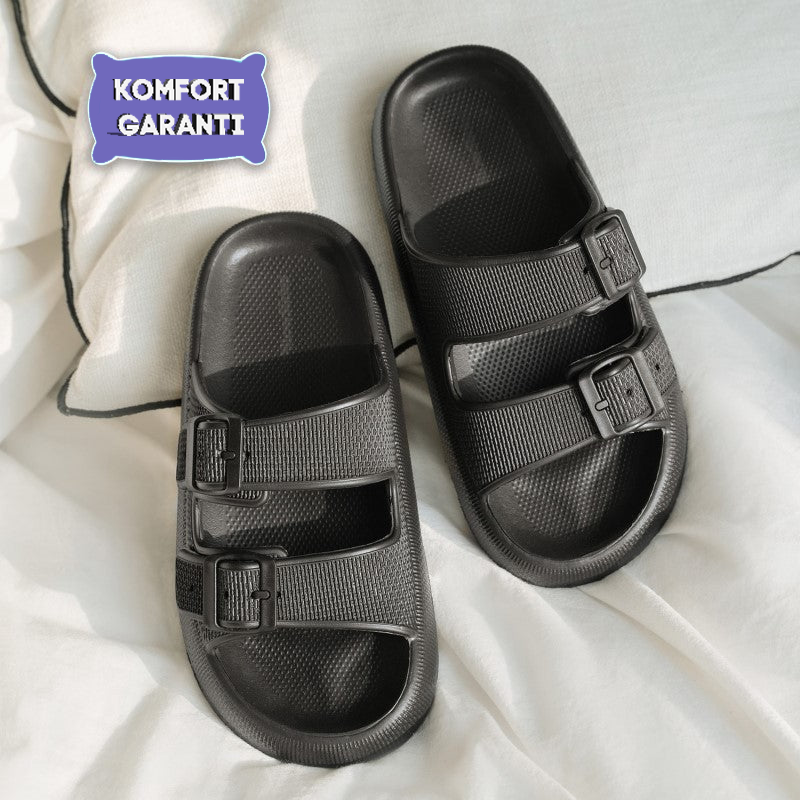 Black ergonomic sandals with adjustable straps on a white background, featuring a "Komfort Garanti" label. Comfortable footwear for everyday use.