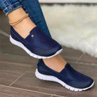 Women's casual navy blue slip-on sneakers with white soles, worn with jeans. Comfortable, stylish footwear for everyday wear.