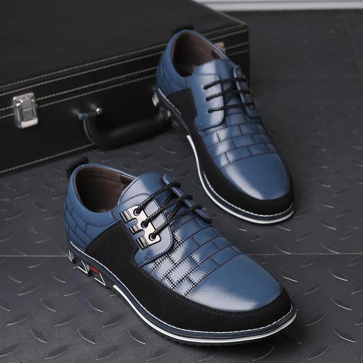 Blue leather men's dress shoes with black accents, lace-up design, and textured pattern, placed on a metal floor near a black suitcase.