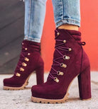 Women's burgundy suede high-heeled boots with gold eyelets and lug soles, paired with blue jeans. Stylish fall fashion footwear.