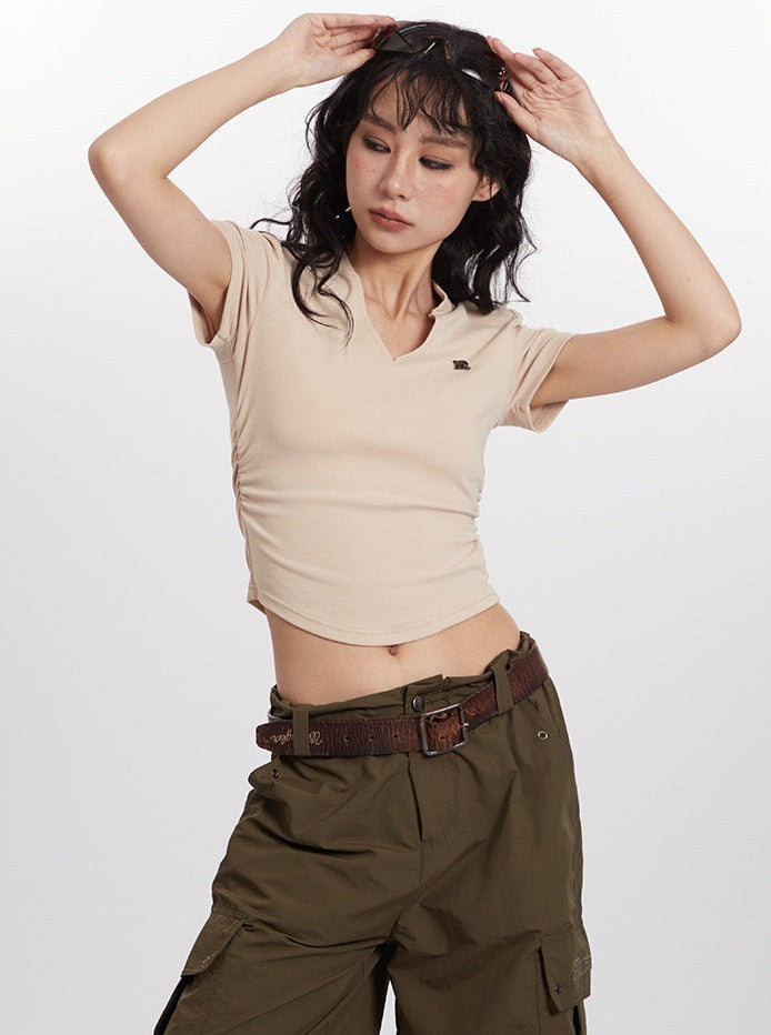 Woman in beige cropped t-shirt and olive cargo pants poses with hands on head, showcasing casual fashion style.