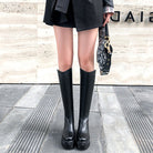 Fashionable black knee-high boots on a woman standing on a city sidewalk, holding a designer handbag. Stylish footwear, urban fashion, women's boots.