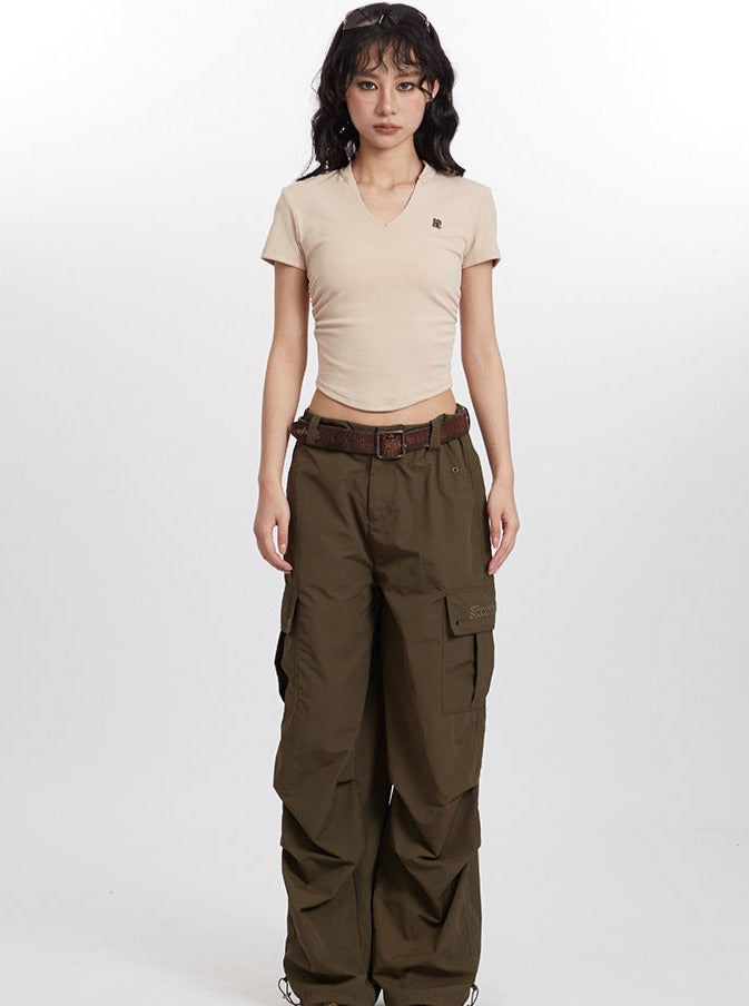 Woman in beige fitted t-shirt and olive cargo pants with brown belt, standing against white background. Fashionable casual outfit, streetwear style.