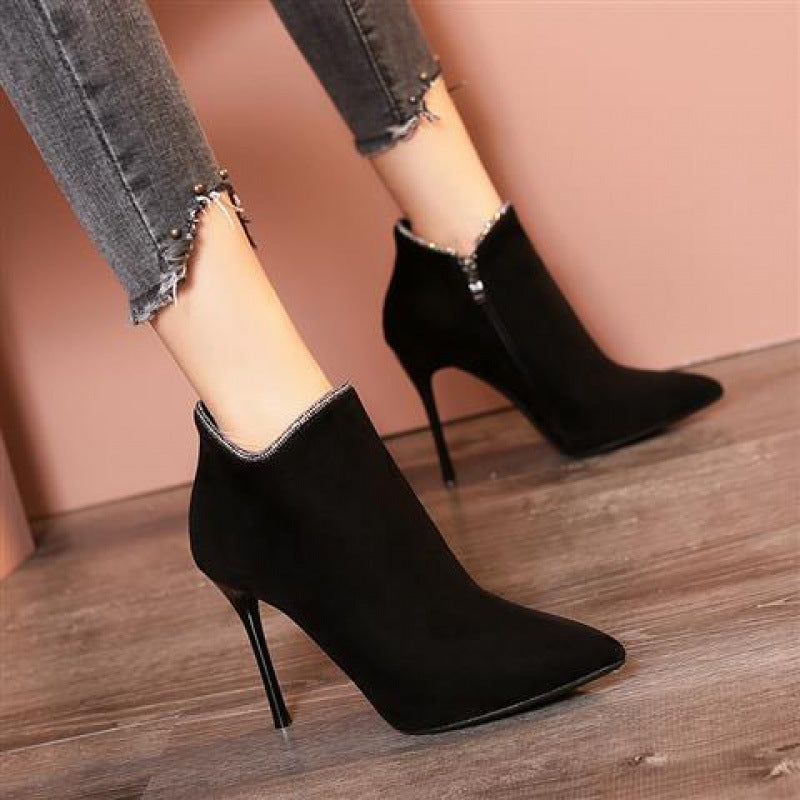 Black suede stiletto ankle boots with pointed toes, worn with frayed hem jeans on wooden floor. Fashionable women's footwear, stylish high heels.