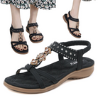 Black women's sandals with rhinestone embellishments, cushioned sole, and floral dress background. Stylish summer footwear for casual wear.