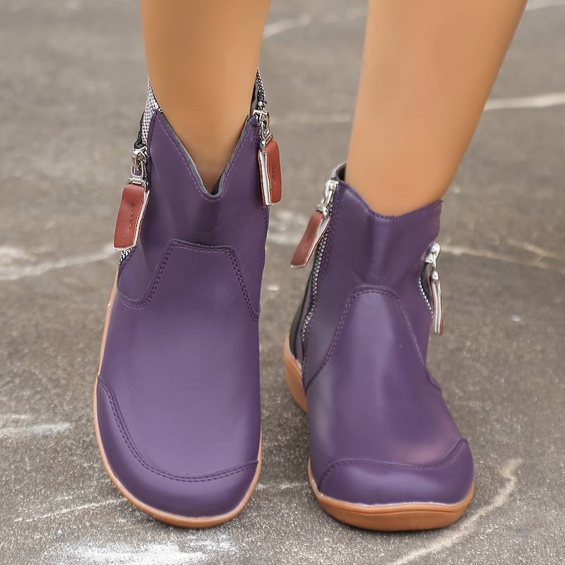 Purple leather ankle boots with side zippers and brown soles on a concrete background. Stylish women's footwear, trendy fall fashion boots.